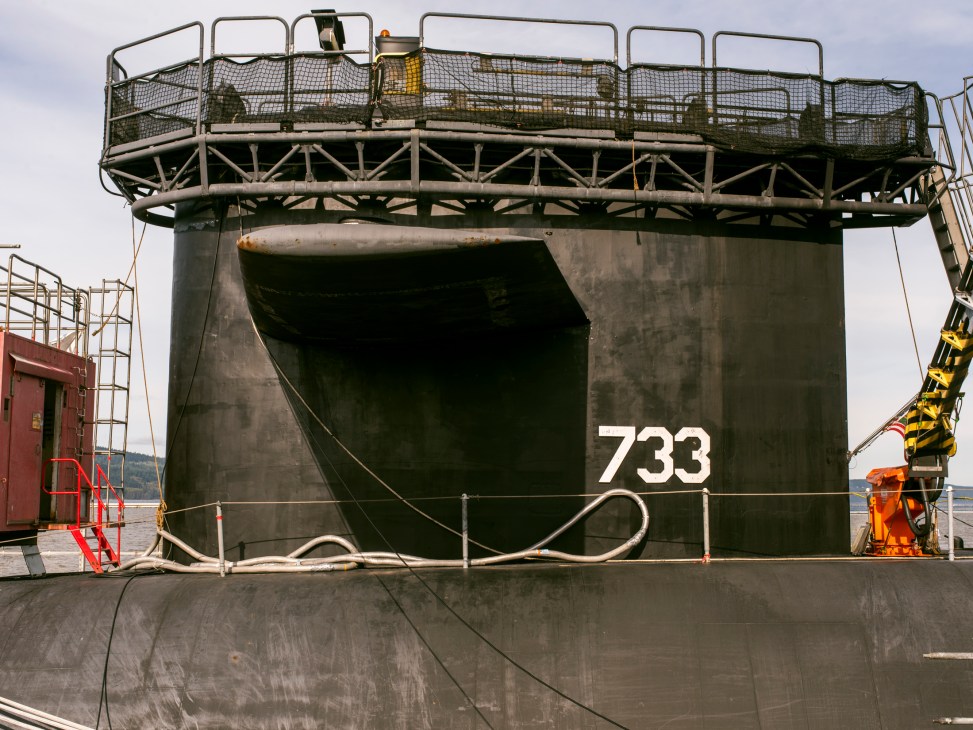 Rear view of USS Maine submarine numbered 733 docked at Naval Base Kitsap with service platforms and equipment visible.