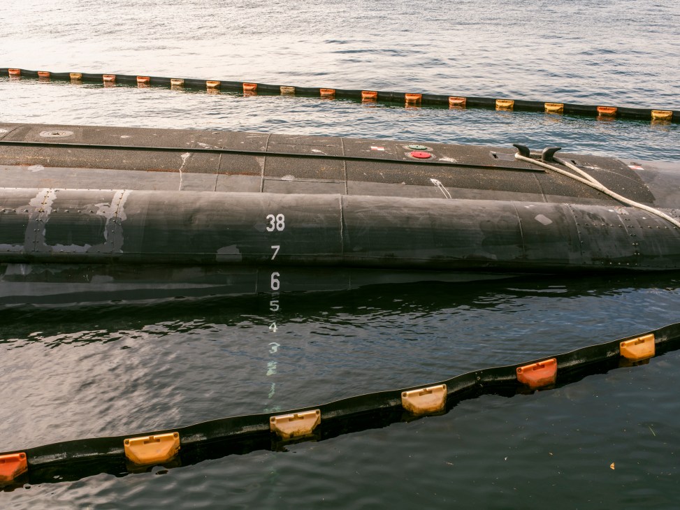 Nuclear submarine hull numbered 38 docked at pier with orange and black buoys in water.