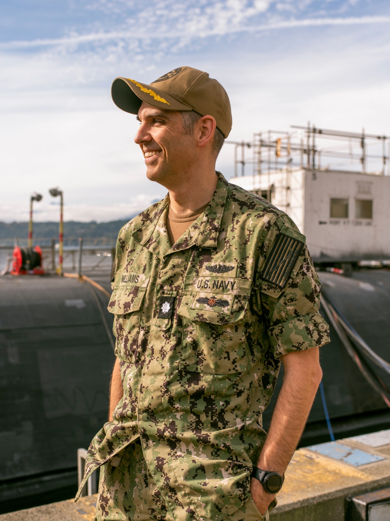 US Navy repair officer Josh Williams in digital camouflage uniform at a naval dock with submarine in background.