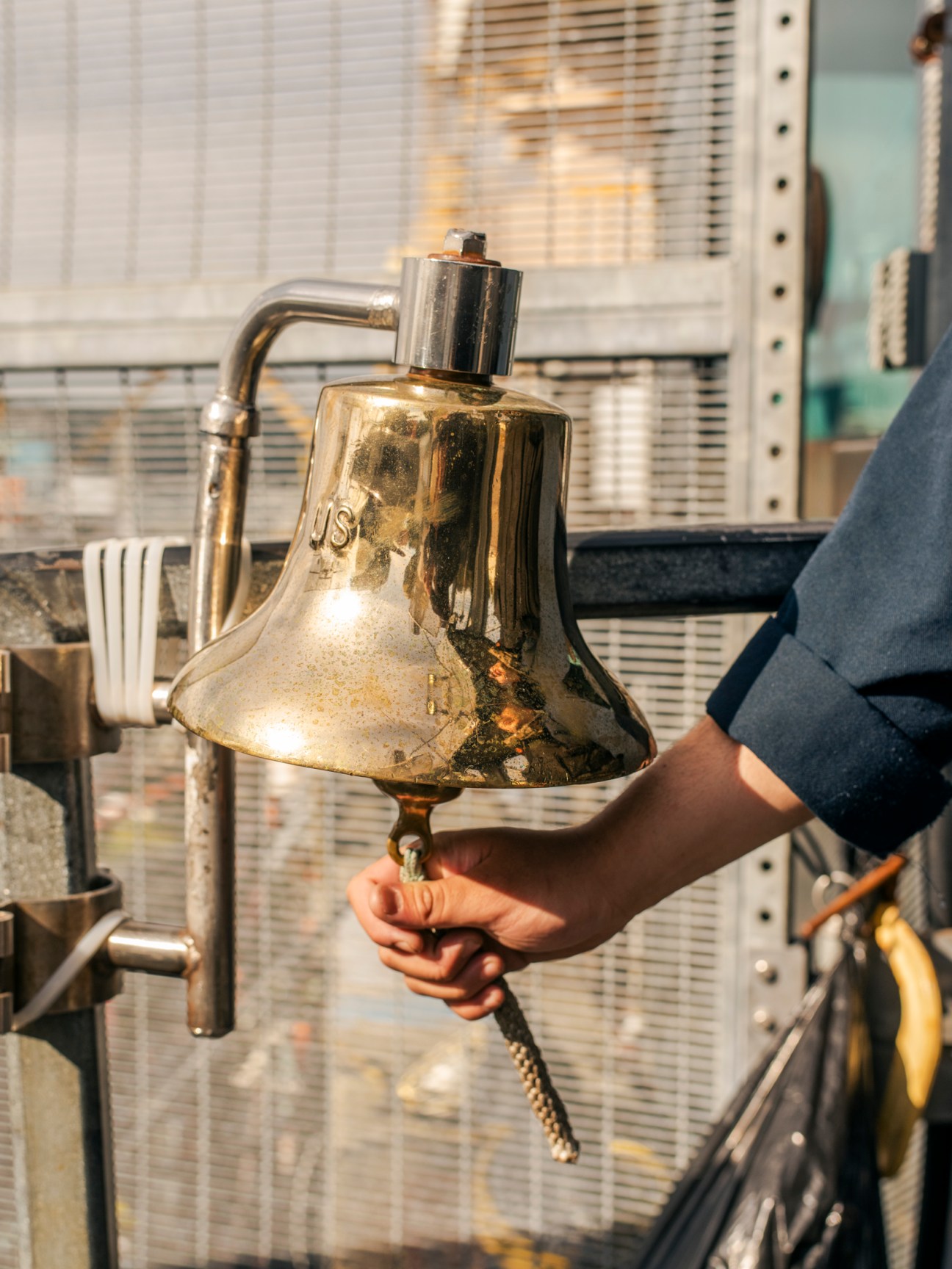 A brass bell with a pull rope being held by a hand inside a submarine interior.