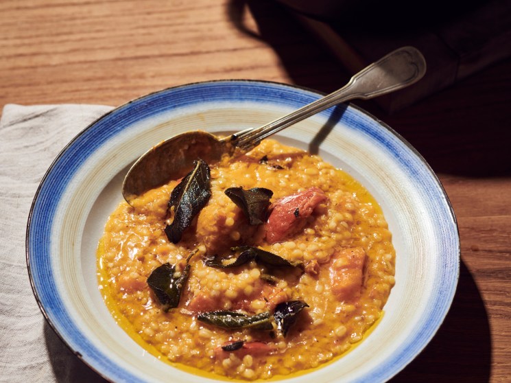 Creamy barley risotto topped with roasted orange pumpkin pieces in a blue-rimmed white bowl