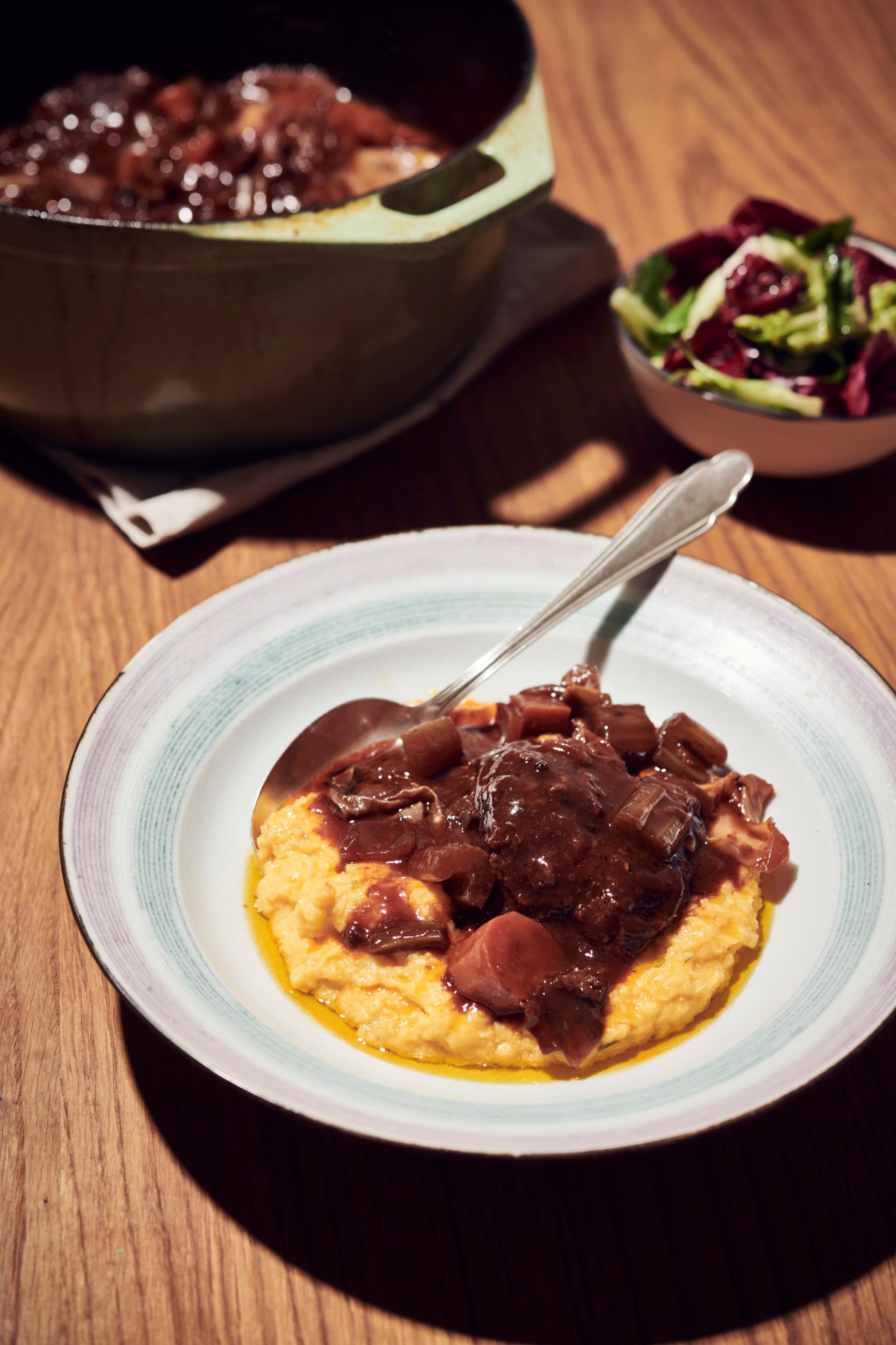 Creamy polenta topped with dark braised meat and mushroom sauce, served with a fork on a white plate