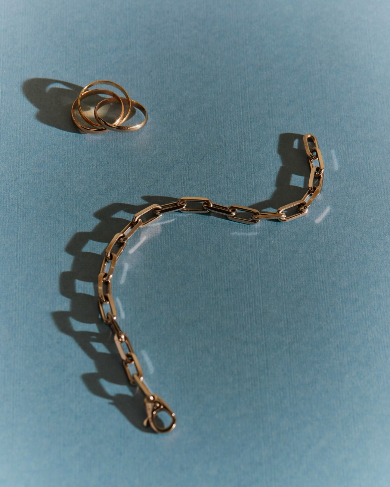 Gold Cartier chain link bracelet and three stacked rings on blue textured surface with dramatic shadows