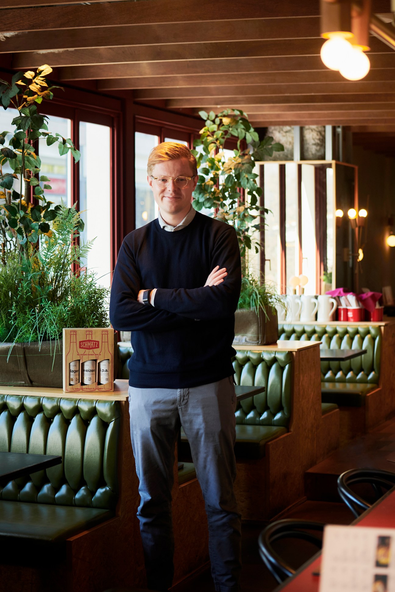 Marc Luetten standing with crossed arms in Schmatz restaurant interior with green booth seating and plants