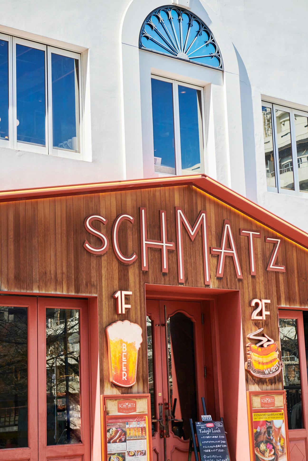 Two-story white building with arched windows and decorative fan window, wood-clad ground floor with red Schmatz signage