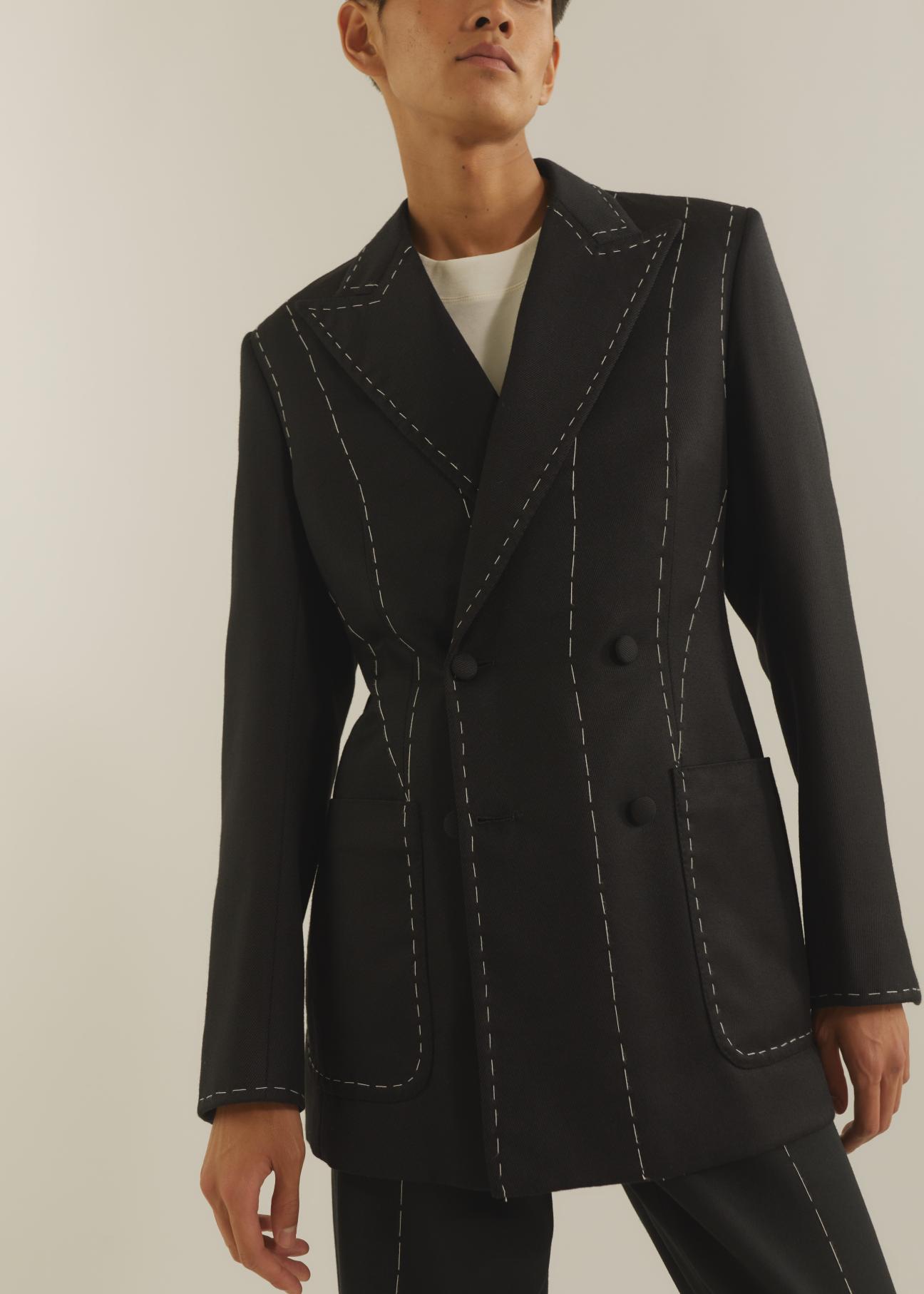 Person wearing a black double-breasted blazer with white topstitching detail from Daniel W Fletcher X Huntsman collaboration