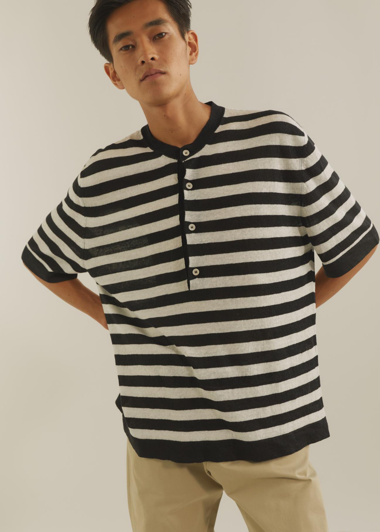Man wearing black and white striped henley shirt with beige trousers