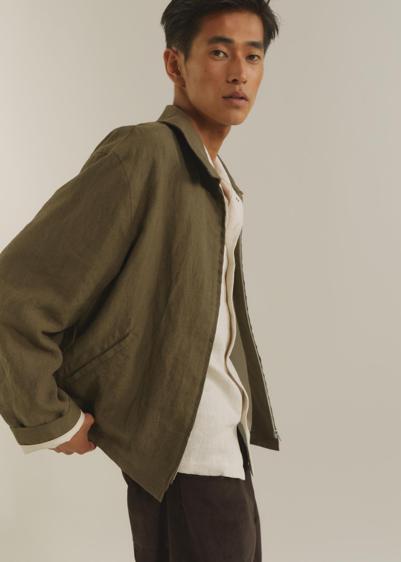 Asian man wearing olive green bomber jacket over white t-shirt against neutral background
