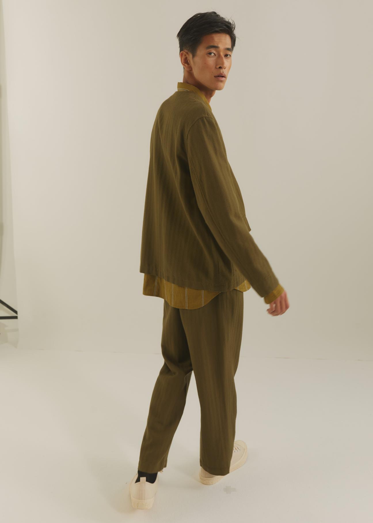 Man in olive green matching suit jacket and pants with yellow shirt underneath