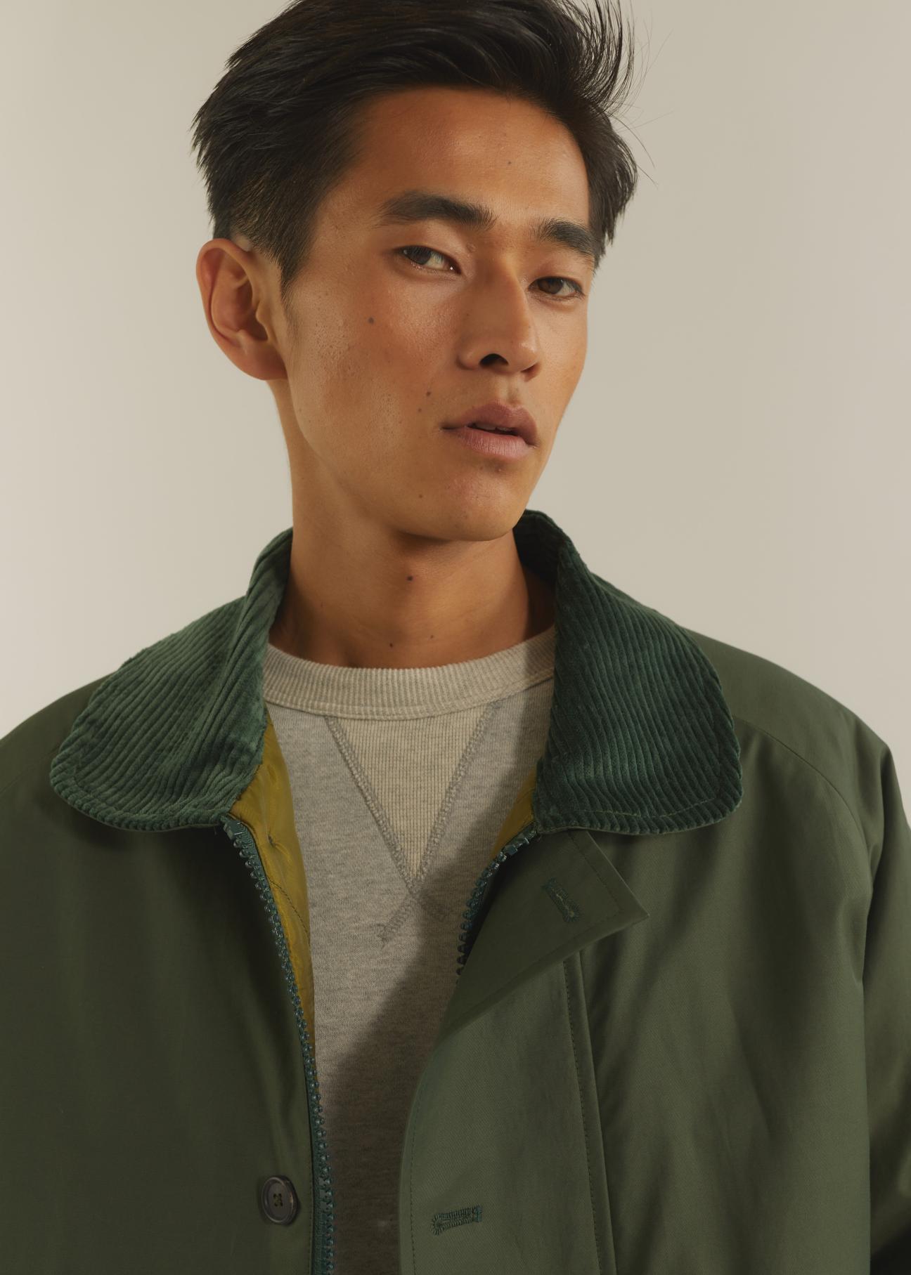 Man wearing green corduroy-collared jacket over light sweater in neutral tones