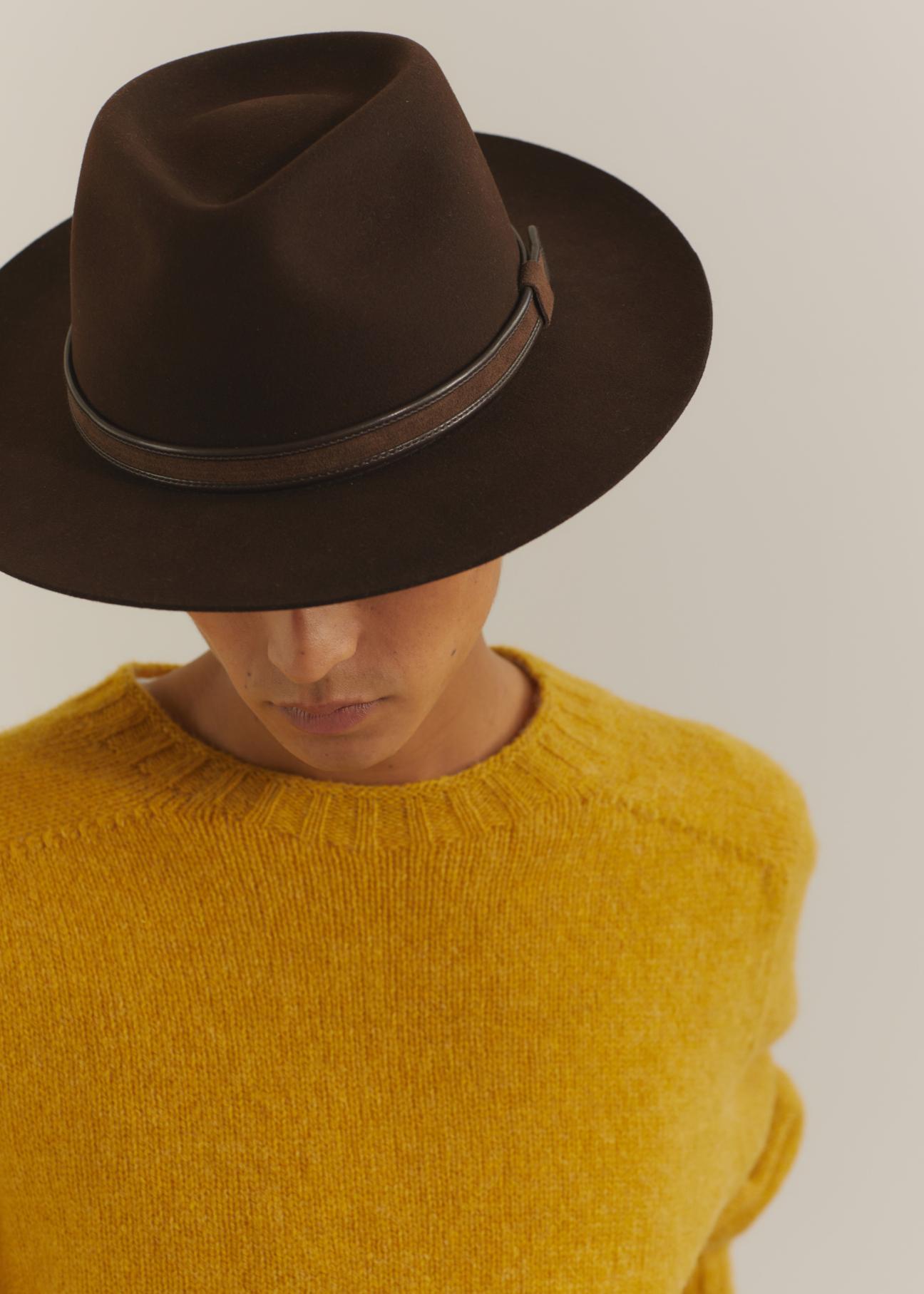 Person wearing brown wool fedora hat and yellow knit sweater