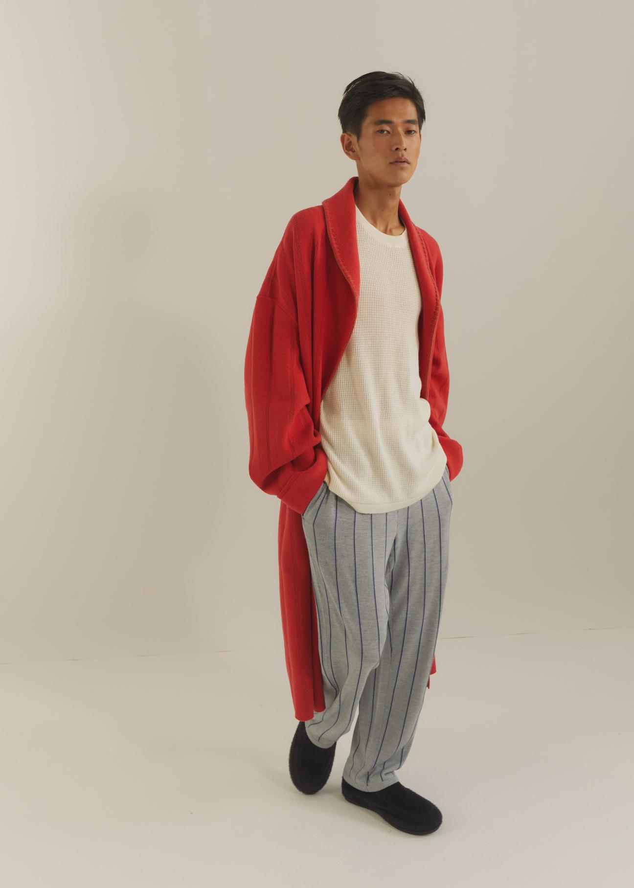 Man wearing red long coat over white shirt and striped trousers against neutral background