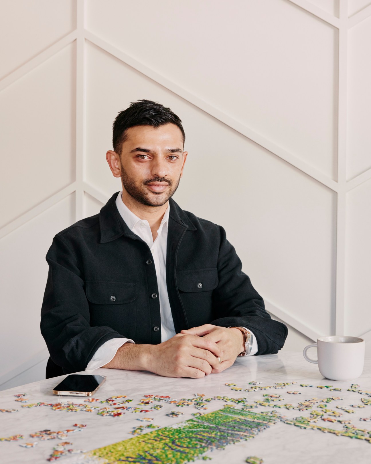 Media entrepreneur Ashish Patel sitting at a white table with puzzle pieces, wearing a dark jacket over white shirt