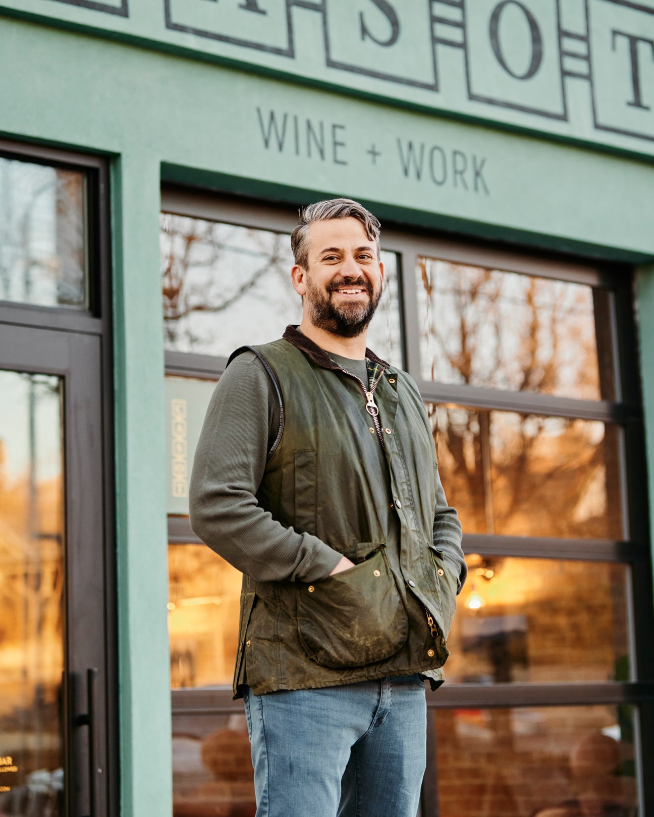 Scott Evans, restaurateur, smiling man with beard standing outside green building with Wine + Work signage