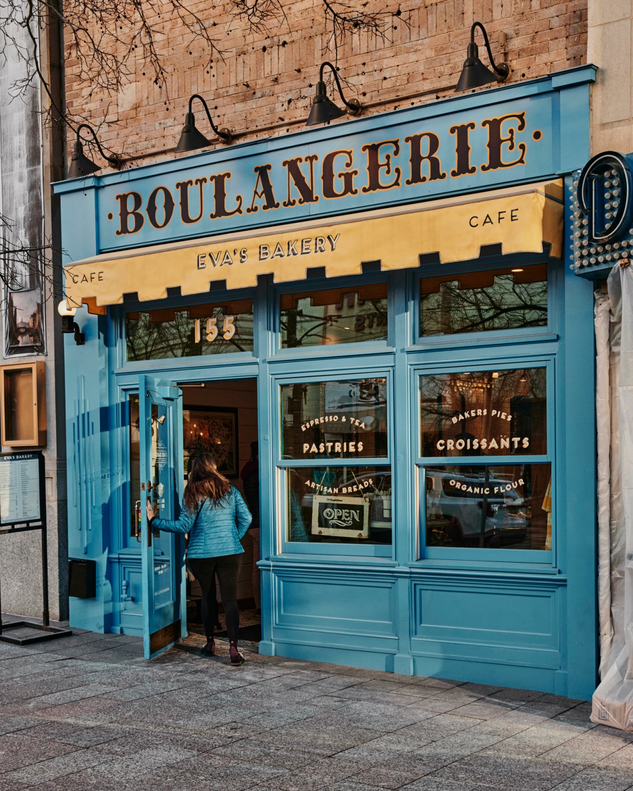 Blue storefront of Eva's Bakery with large windows, vintage signage, and person entering the cafe