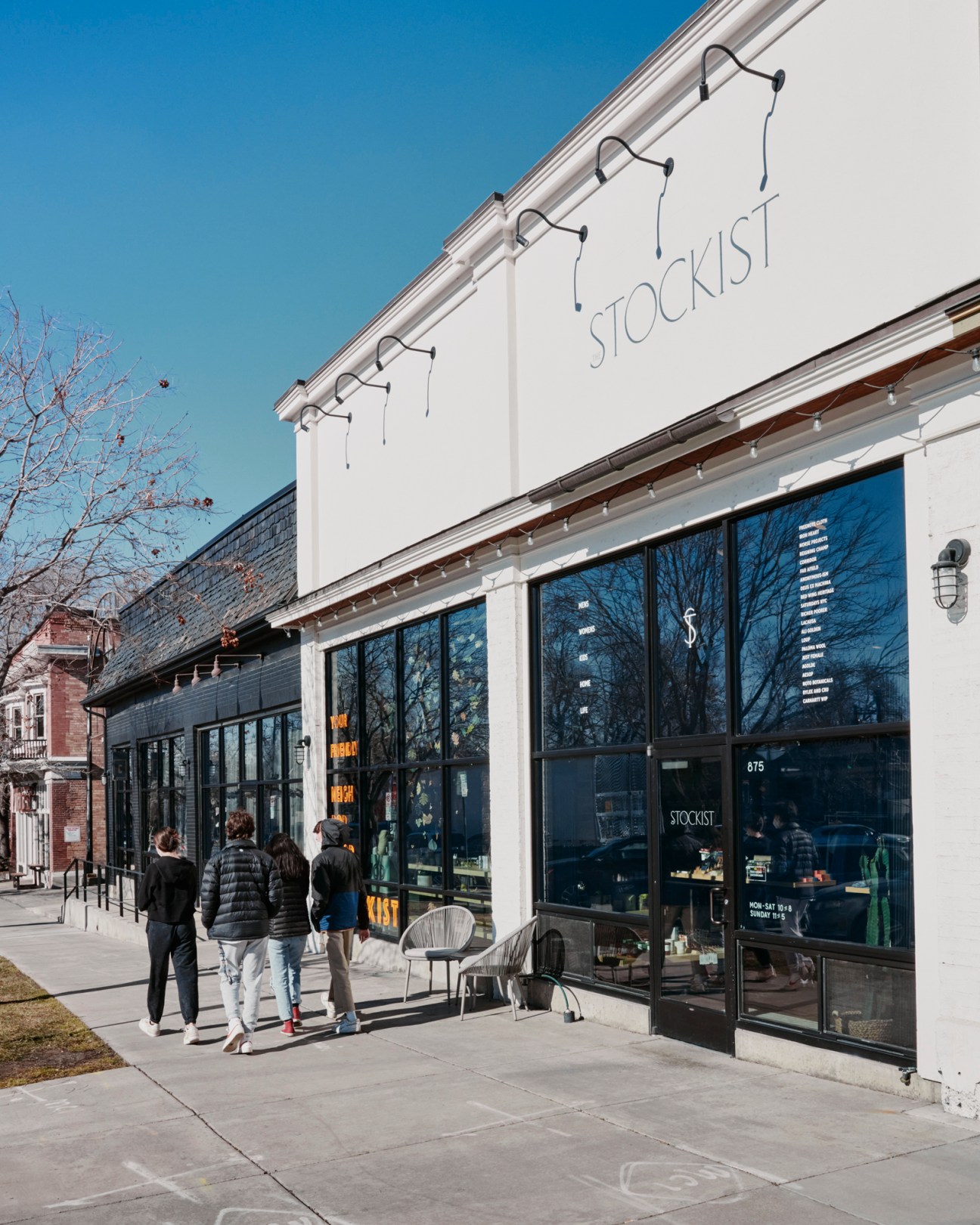 White storefront building with large windows displaying Stockist store signage, people walking on sidewalk