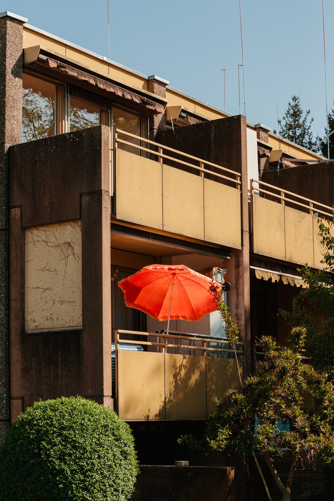 Person holding a bright red umbrella on a modernist building balcony during sunny weather.