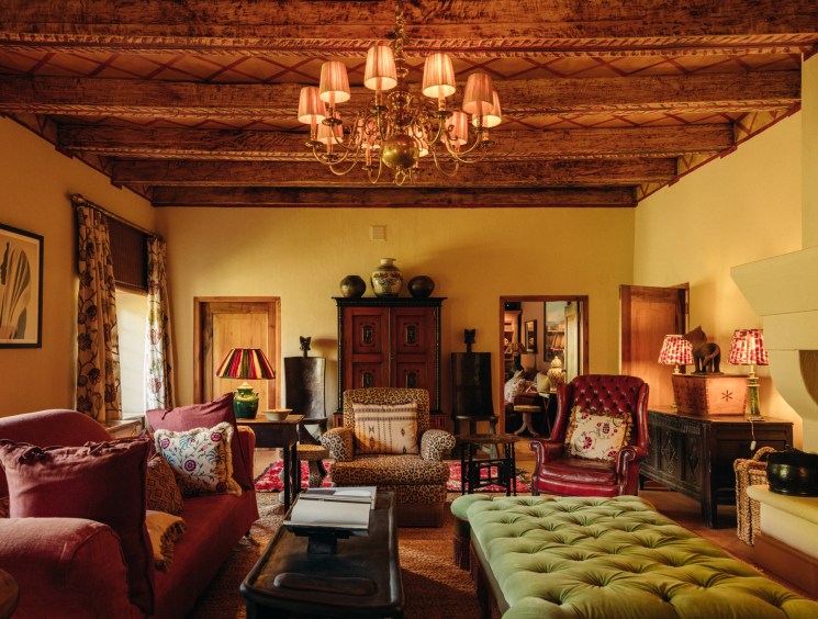 Rustic living room with exposed wooden ceiling beams, chandelier, burgundy armchairs, and fireplace