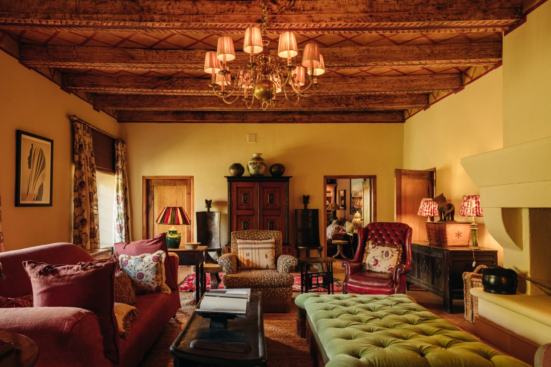 Rustic living room with exposed wooden ceiling beams, chandelier, burgundy armchairs, and fireplace
