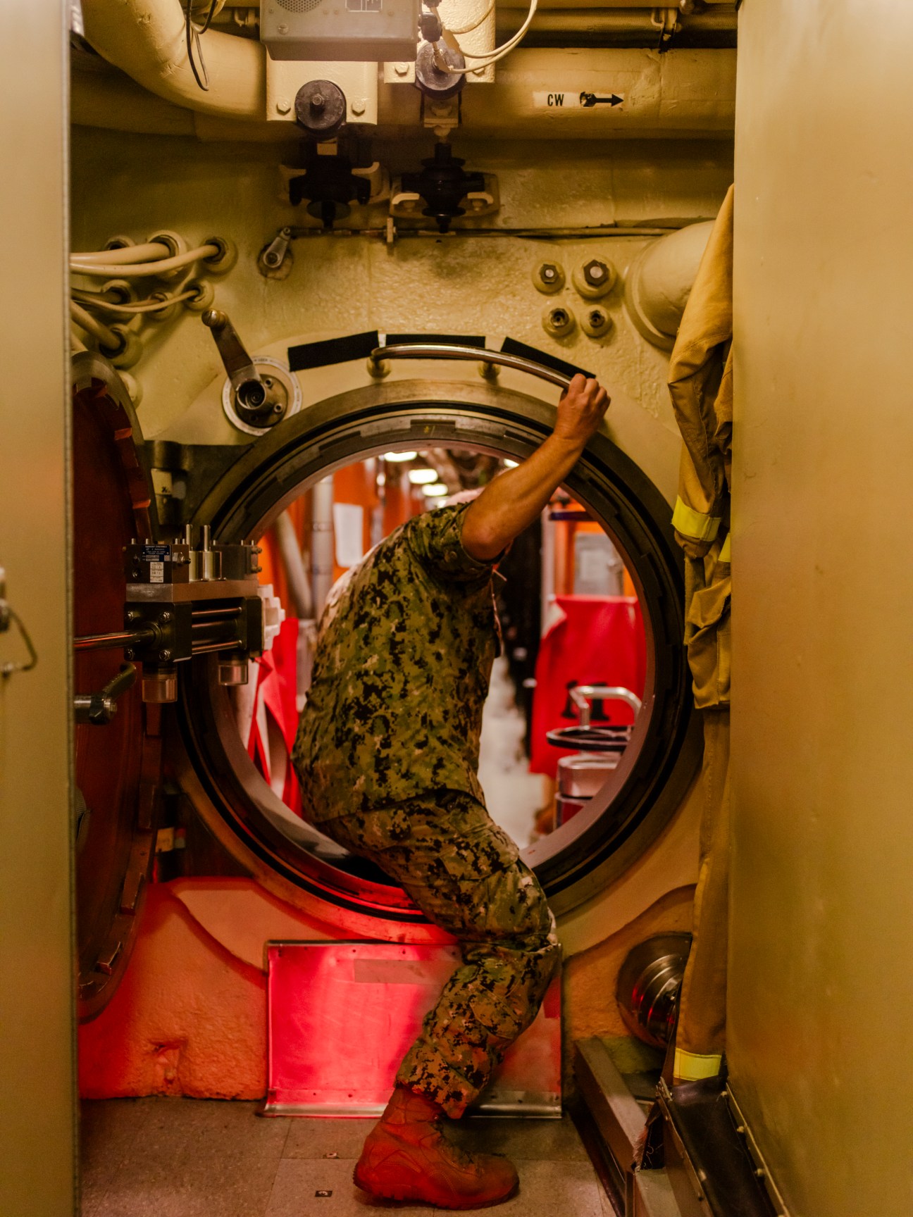 A U.S. Navy sailor in camouflage uniform works through a submarine hatch opening in the USS Maine's cramped interior.