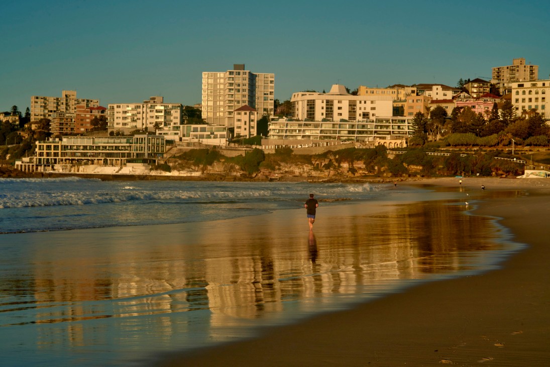 Person jogging alone on wet beach with their reflection visible in the sand at golden hour