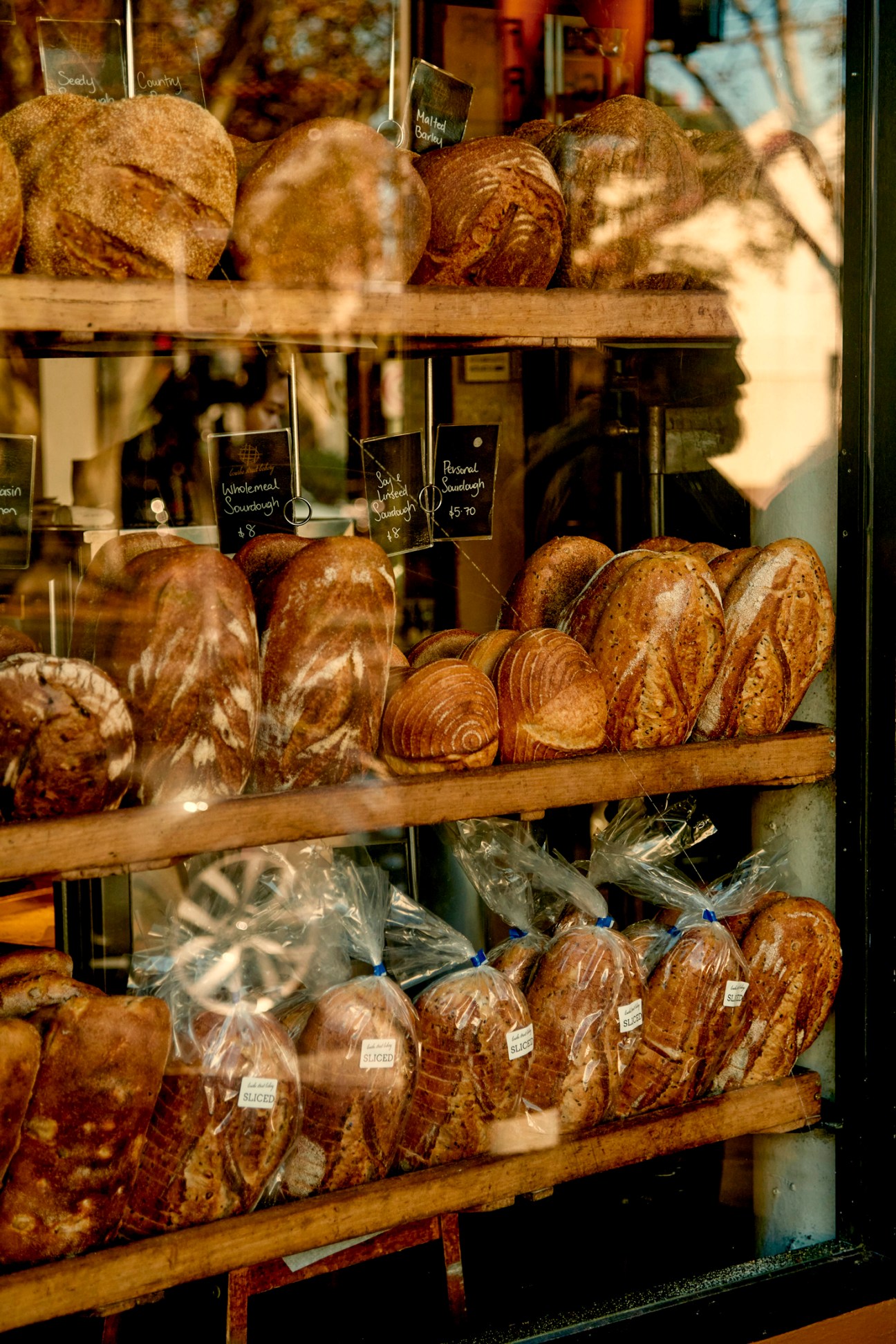 Display window showing various artisanal bread loaves on wooden shelves with price tags in a bakery