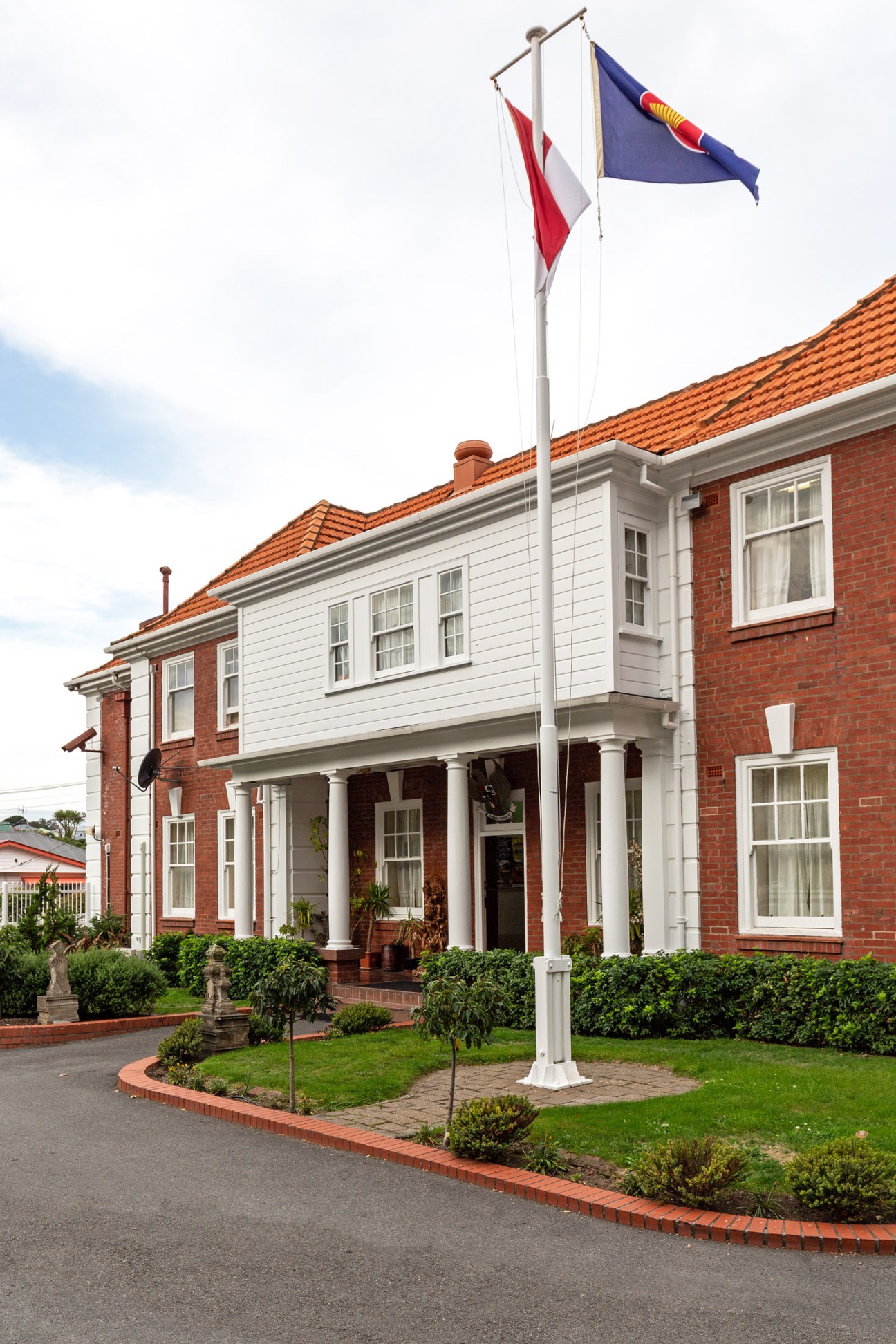 Red brick diplomatic building with white trim and Indonesian and Polish flags flying from a pole