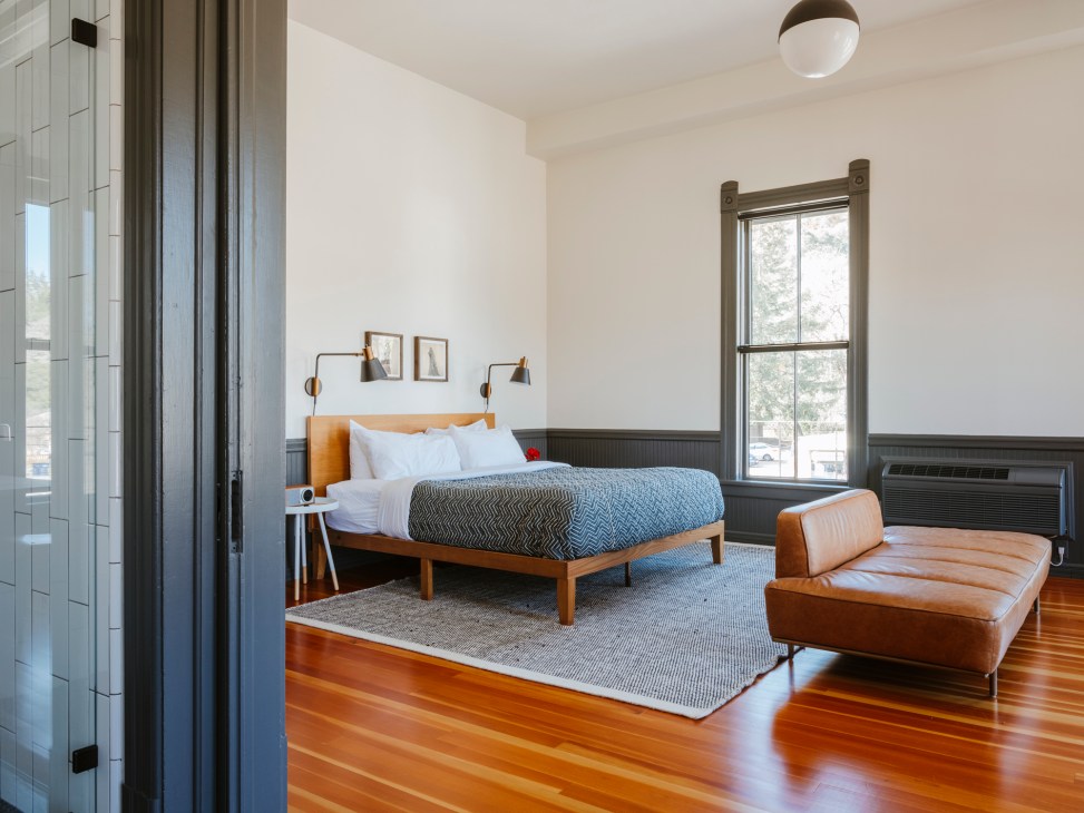 Modern hotel room with wooden bed frame, white bedding, leather bench, and hardwood floors