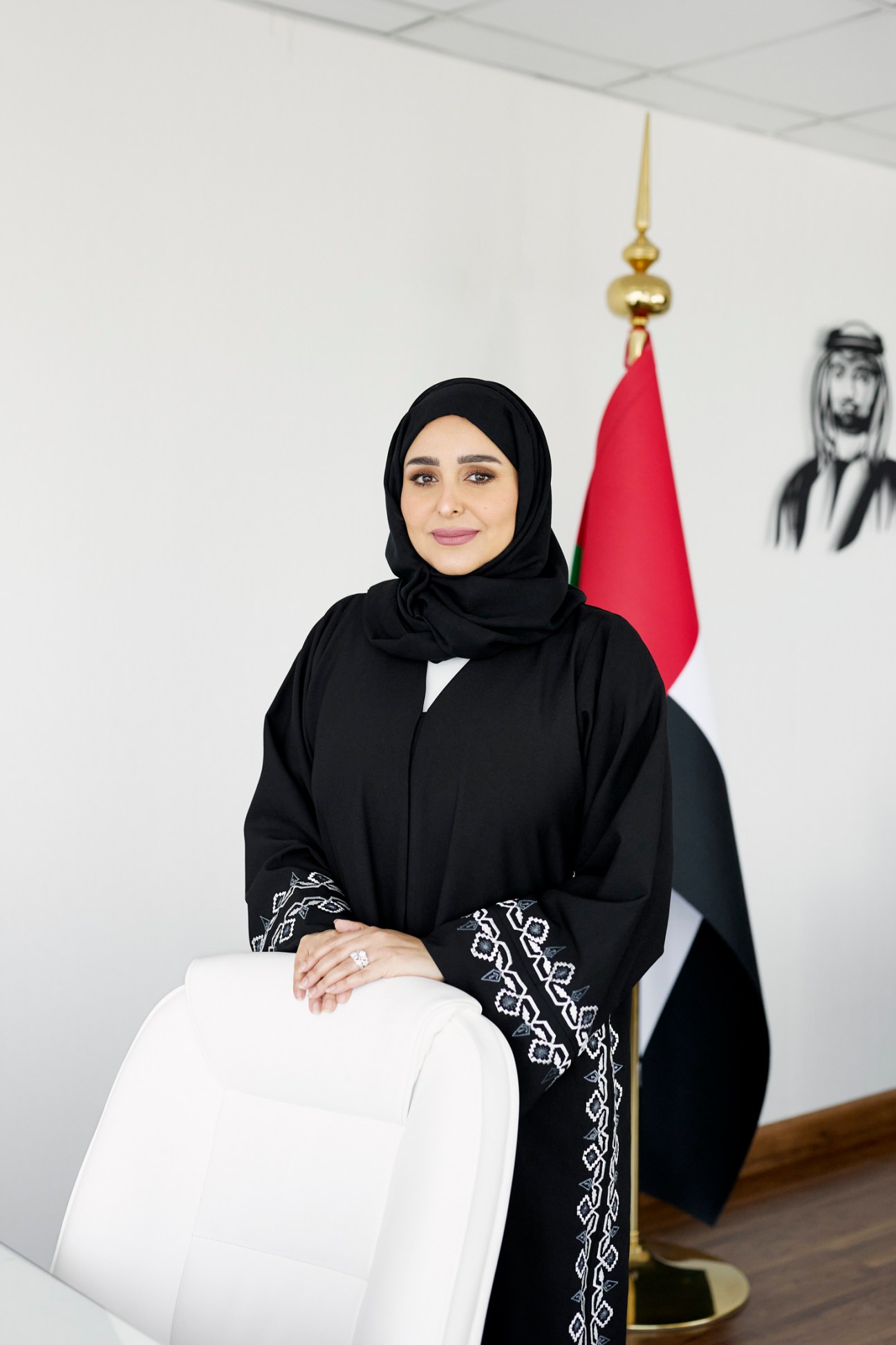 Dina Fares, director of digital transformation at Ajman Digital Government, poses in professional black abaya with UAE flag in background.