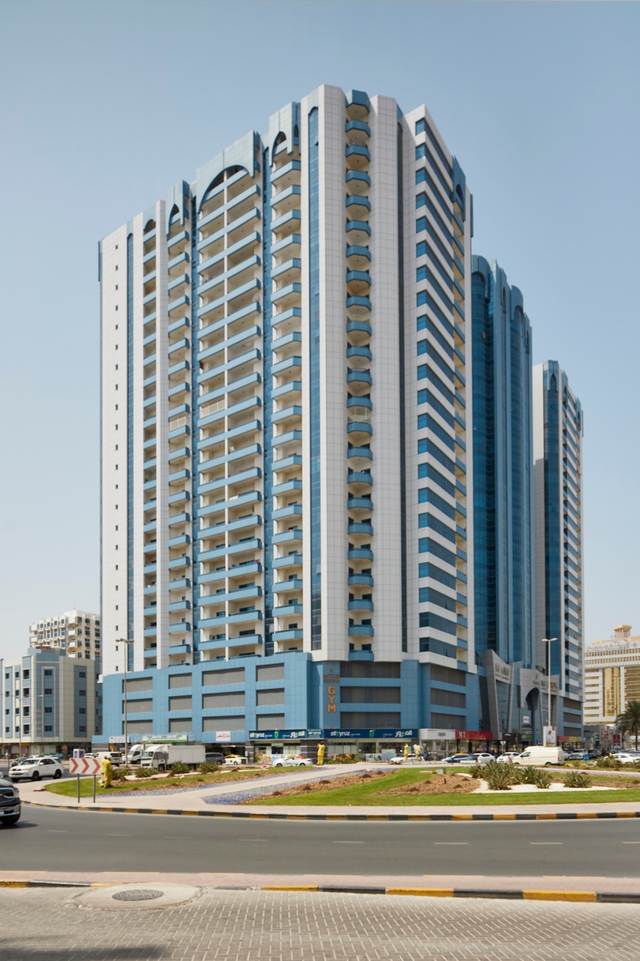 Modern multi-story residential tower with blue and white facade and ground-level commercial spaces in UAE.