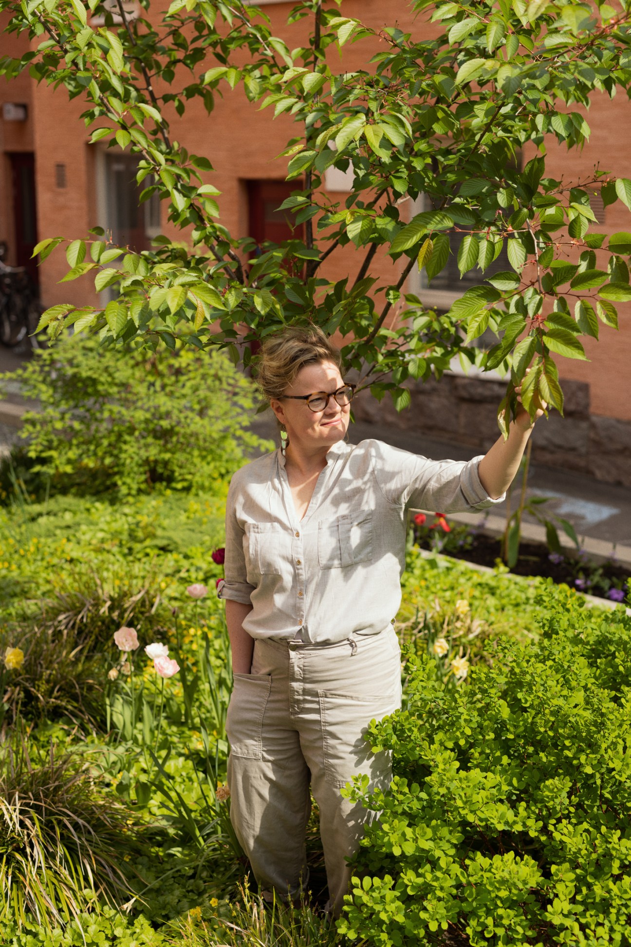 Kaisa Viitanen reaching up to touch tree branches in a green courtyard garden with lush vegetation