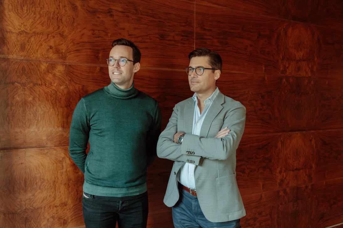 Niels Lehmann and Valentin Müller standing against wood-paneled wall, one holding architectural model