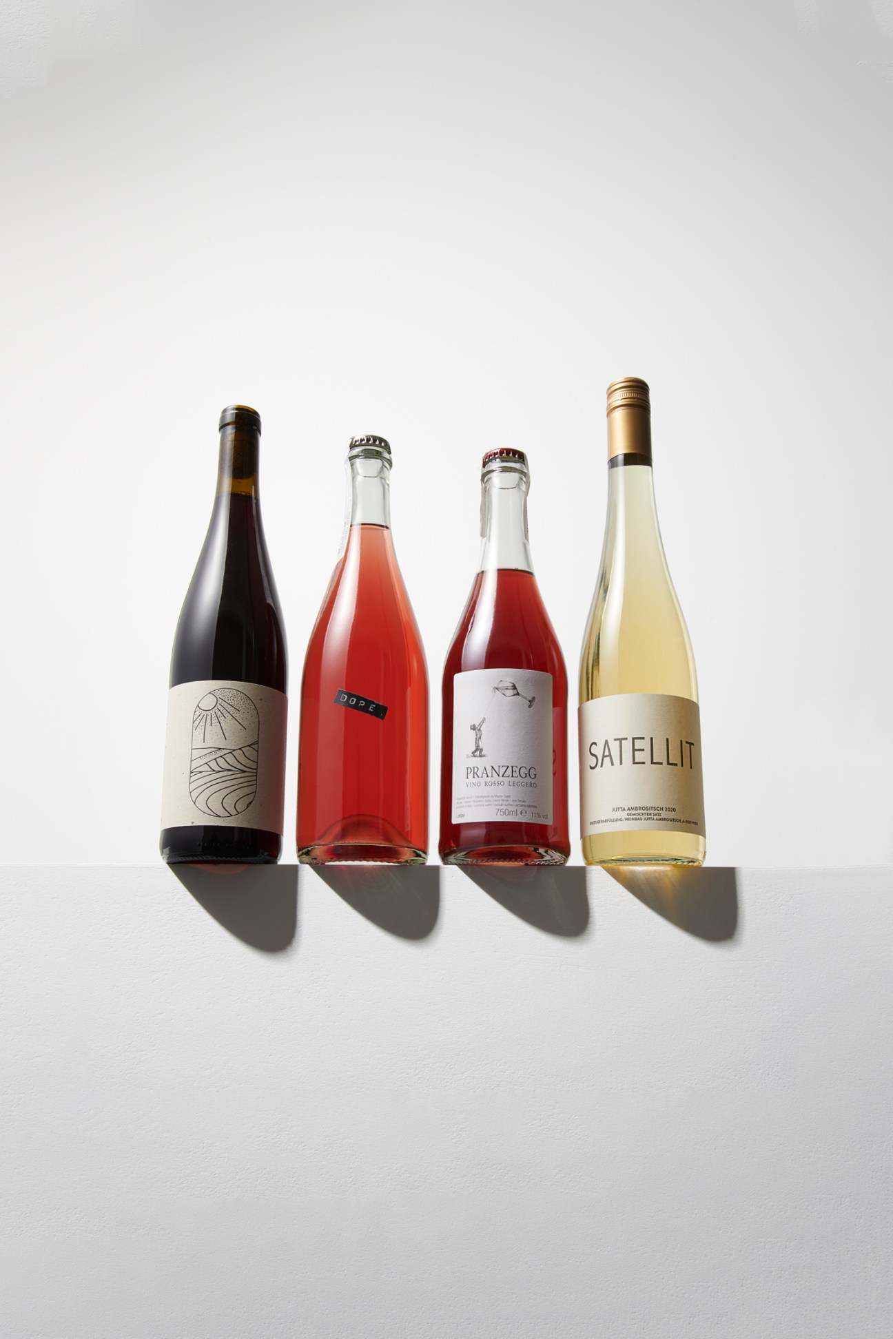 Four wine bottles with minimalist label designs arranged in a row against a white background casting shadows