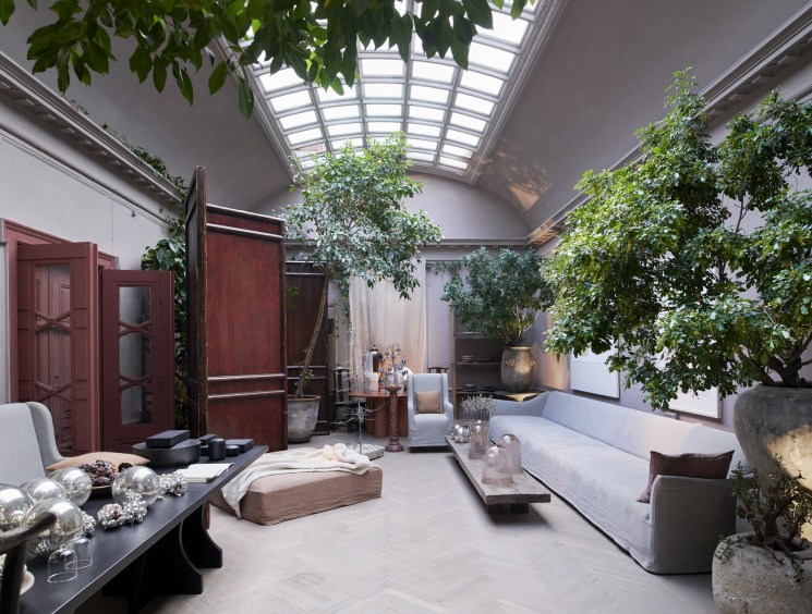 A dramatic loft-style living space with a vaulted skylight ceiling, full-grown indoor trees, and eclectic furnishings.