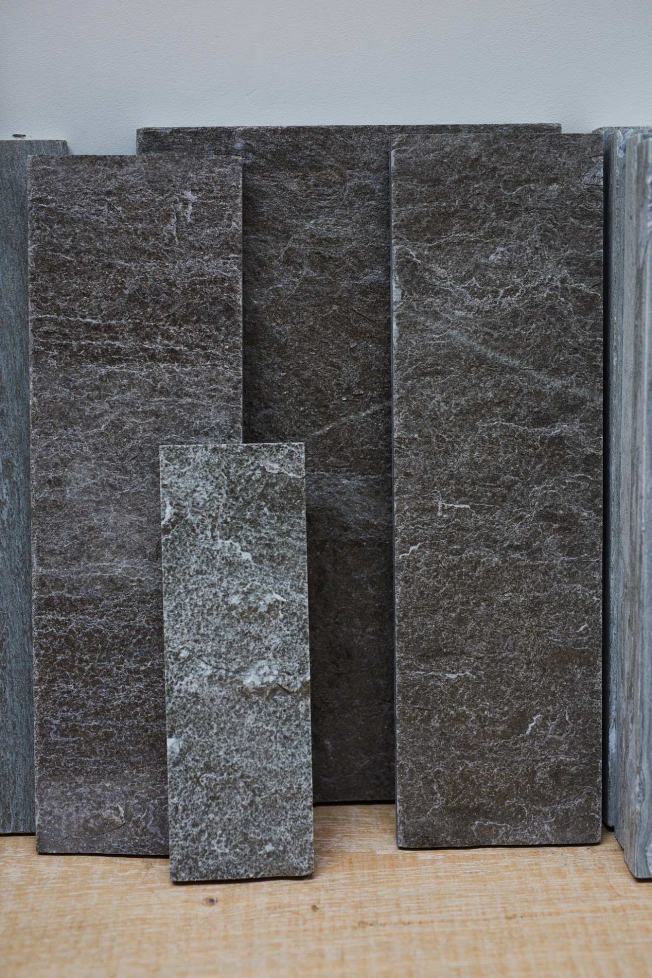 Dark stone slabs with natural veining and texture displayed vertically against white wall