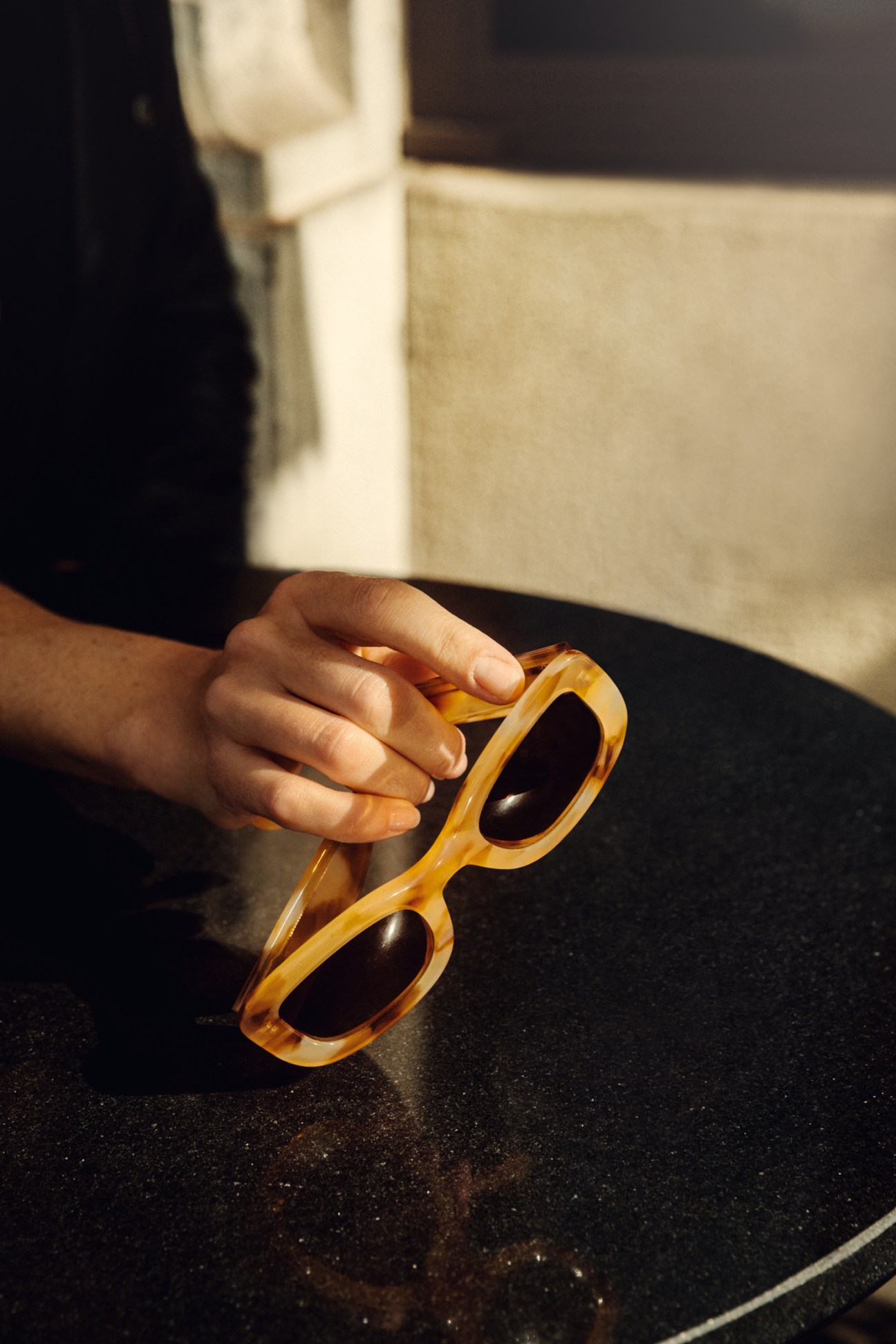 Hand holding amber-colored VIU sunglasses on dark surface