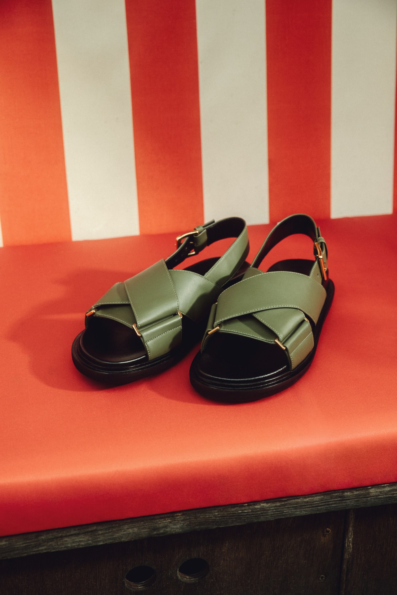 Marni sandals with olive green leather straps and chunky black soles on striped red and white background