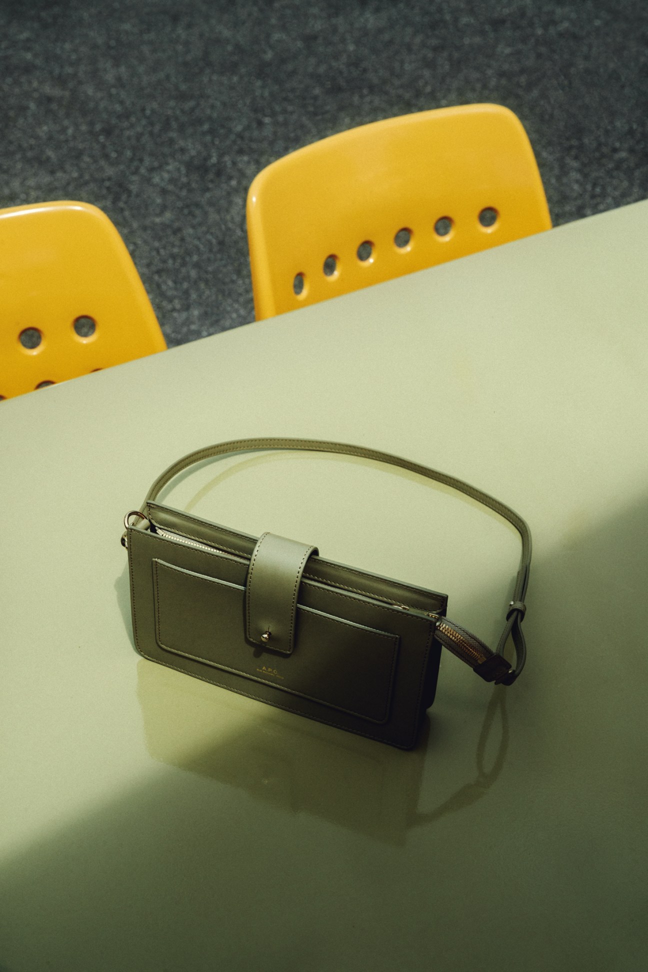 Green leather APC bag with handle and front pocket sitting on white table with yellow chairs in background