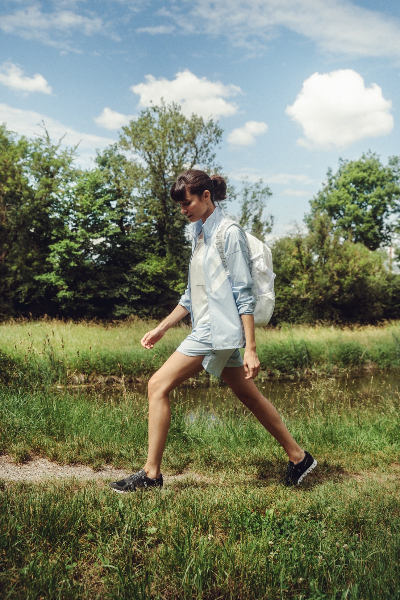 Woman walking outdoors wearing light blue Adidas Terrex jacket and shorts with On sneakers and Adidas backpack