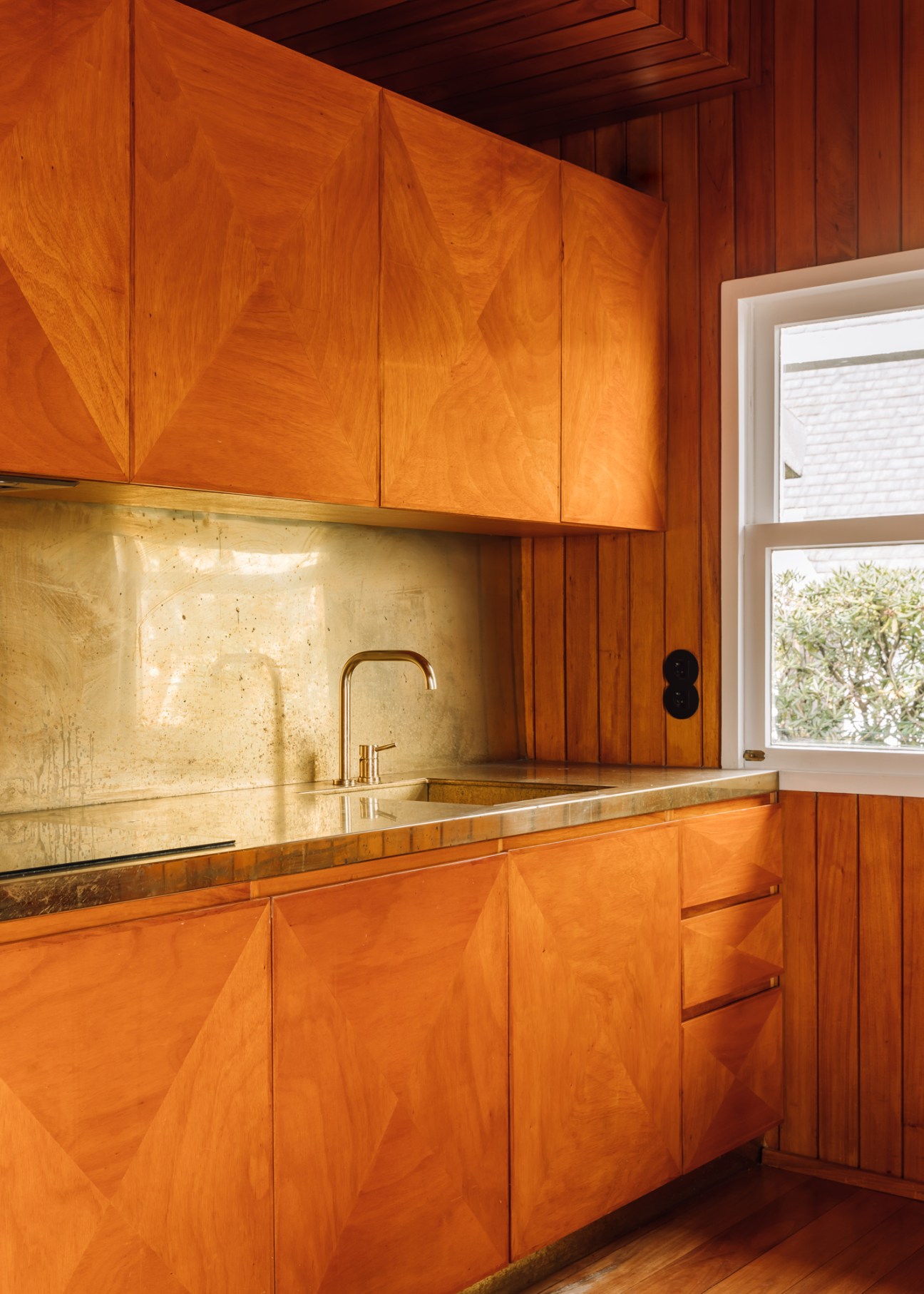 Modern kitchen with wood cabinets, brass backsplash and countertop, white window frame
