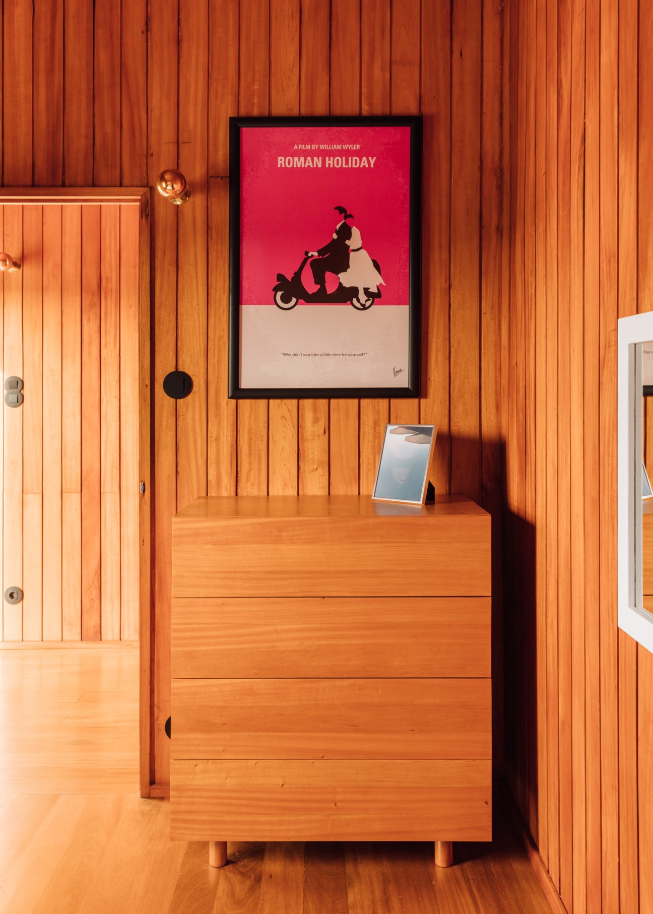 Wood dresser with drawers against wooden wall panels with Roman Holiday movie poster