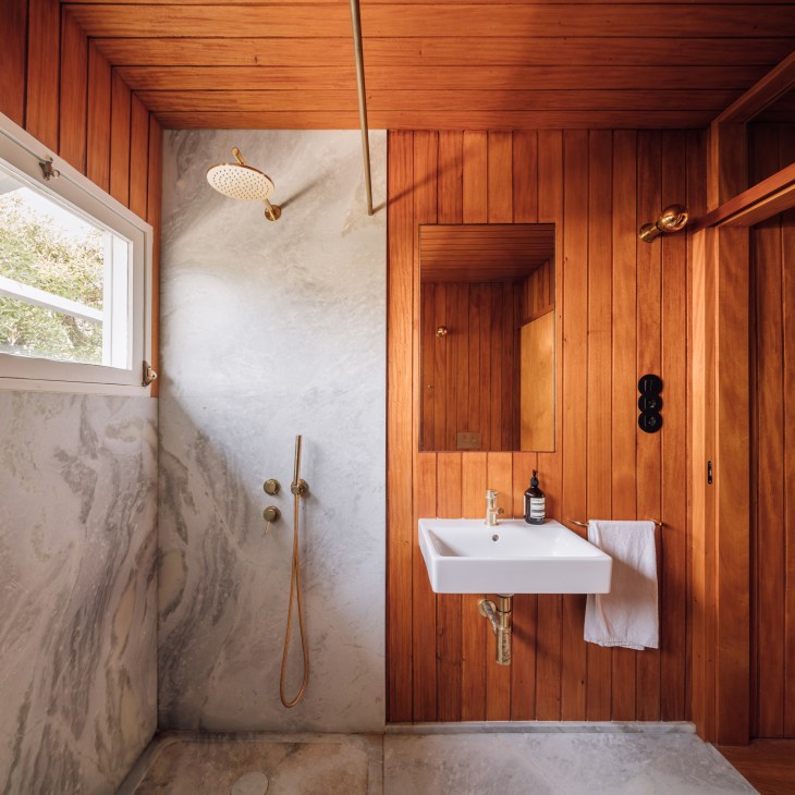 Bathroom with wood-paneled walls, white sink, brass fixtures, and marble shower area with blue-green veining