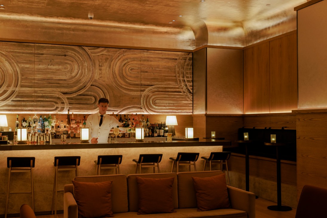 Elegant hotel bar with warm wood paneling, curved ceiling details, bar stools, and bartender in white jacket