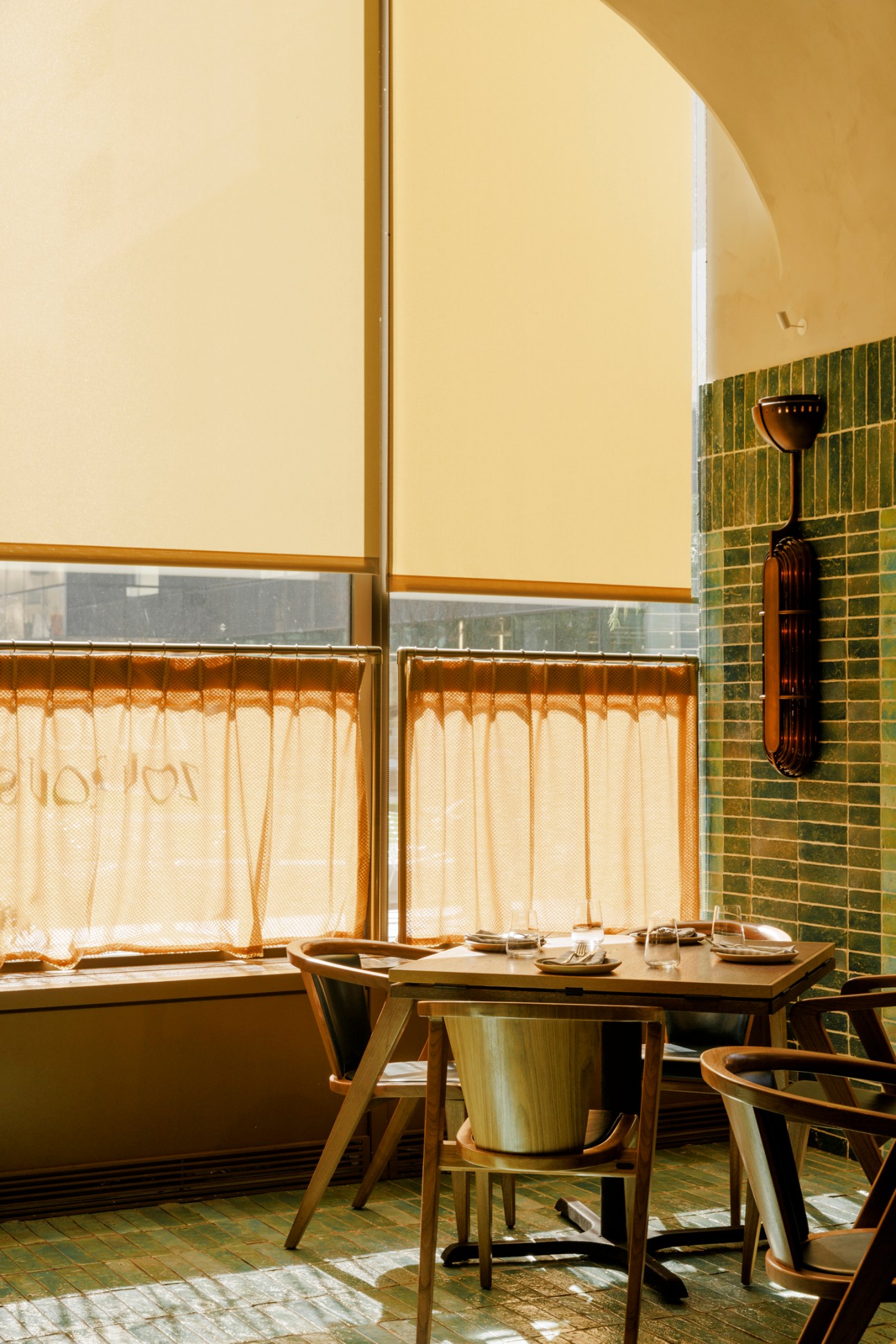 Restaurant table setting with plates and glasses in warm yellow lighting with green tiled wall and decorative vase