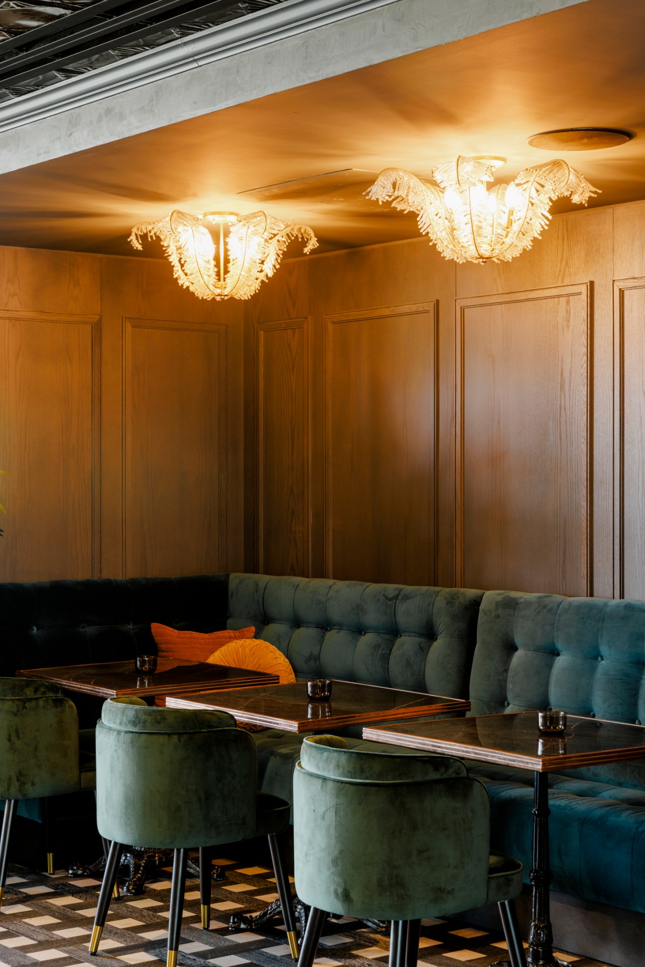 Restaurant dining area with tufted green velvet banquette seating, round tables, and ornate pendant lighting