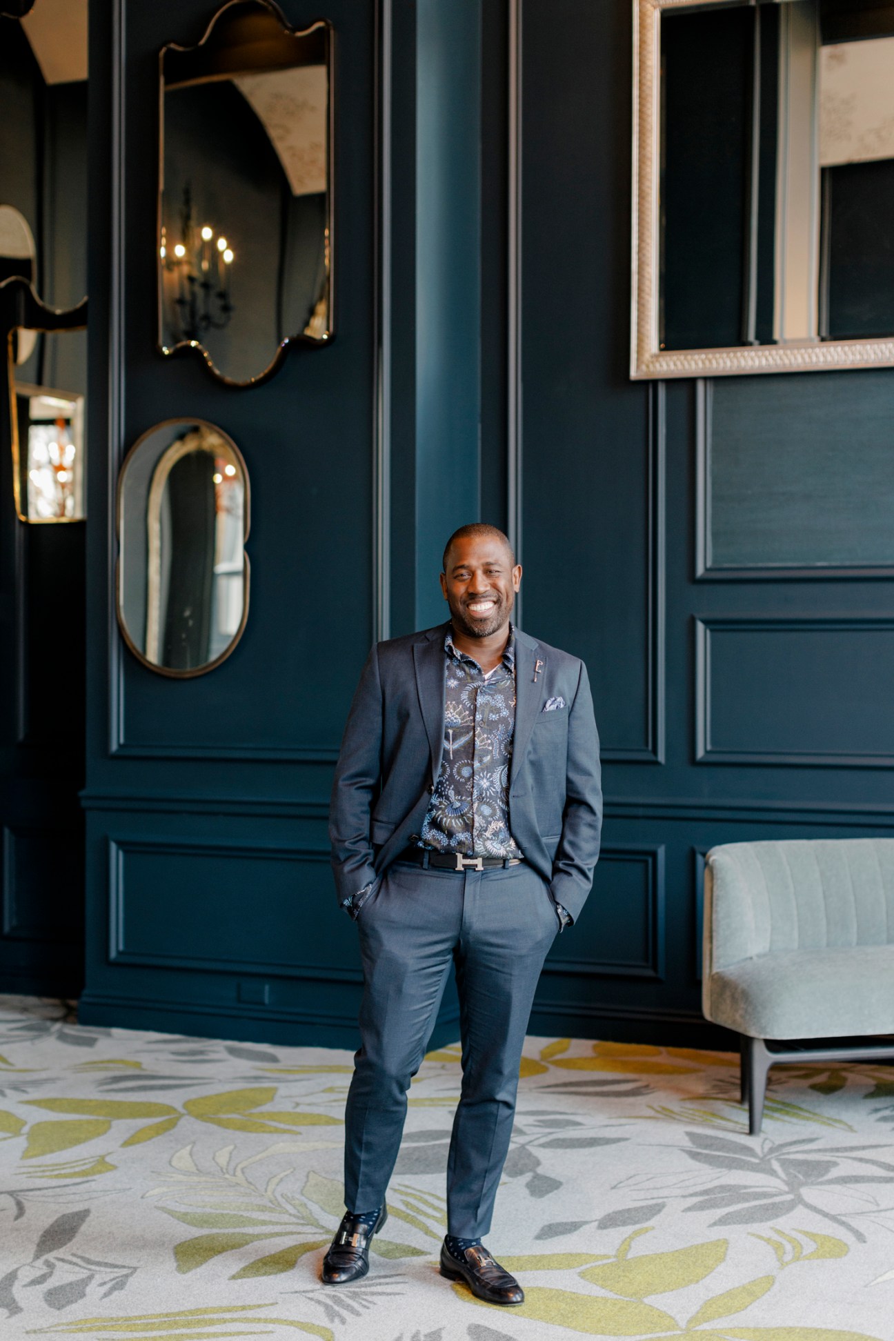 Prince A Sanders standing in an elegantly designed hotel interior with dark blue paneled walls and decorative mirrors