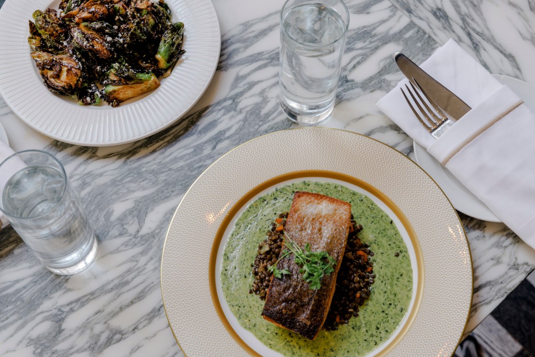 Seared fish fillet with green herb sauce and dark lentils on white plate with gold rim