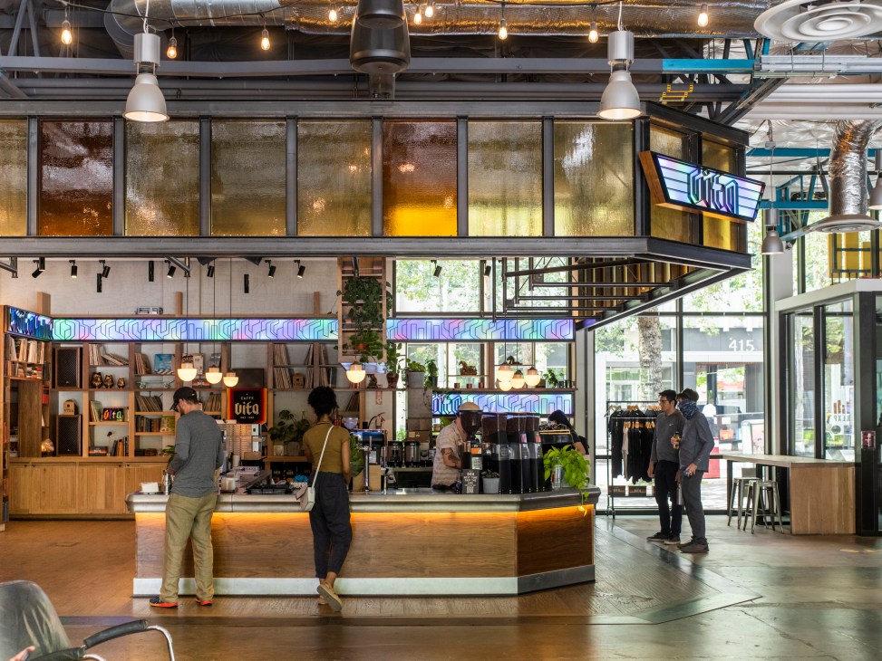 Modern industrial coffee bar with exposed ceiling, pendant lights, and customers ordering at curved counter