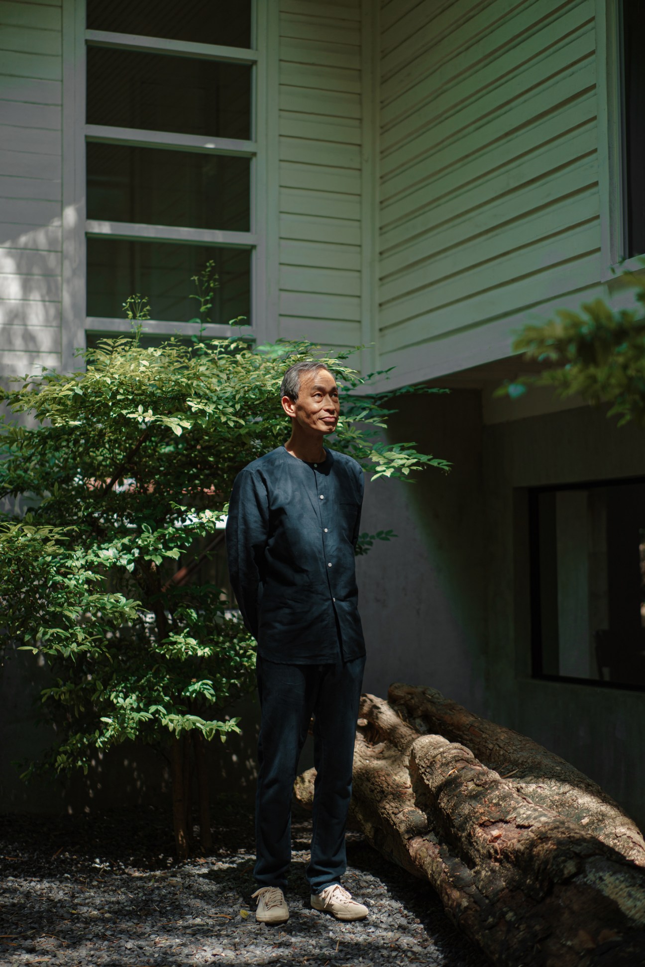 Carlson Chan standing outdoors next to a large fallen log in front of a green wooden building