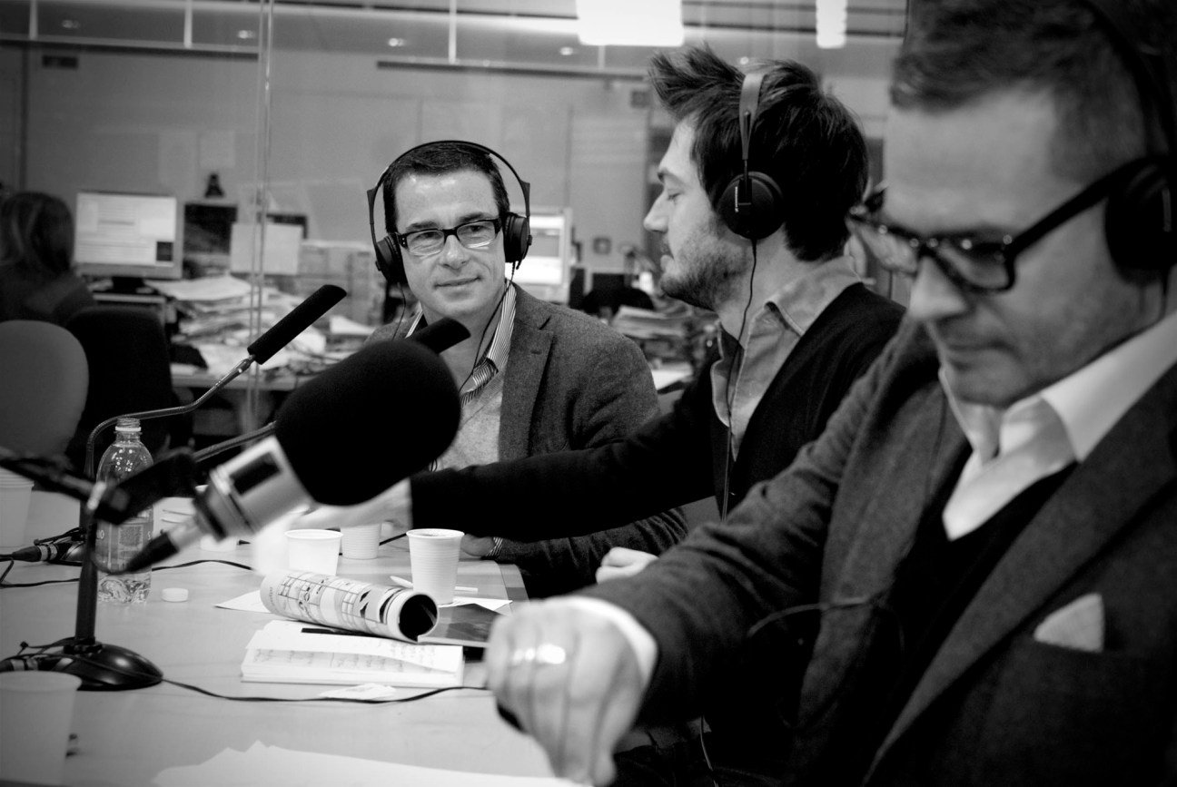 Two men in business attire sitting at radio studio desk with microphones and headphones
